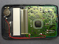 The interior of a newer (c. 2000) pocket calculator. It uses a button battery in combination with a solar cell. The processor is a "Chip on Board" type, covered with dark epoxy.