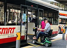 A man on a motorized wheelchair is using a ramp to enter an SMRT bus